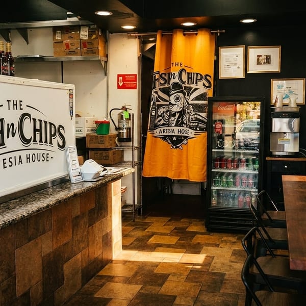 Interior of The Fish 'n Chips Artesia House restaurant, showing counter, seating, and kitchen area.