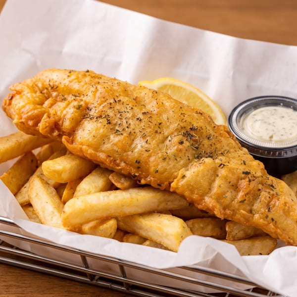 Golden-brown fish and chips in a metal basket with a lemon wedge and tartar sauce.